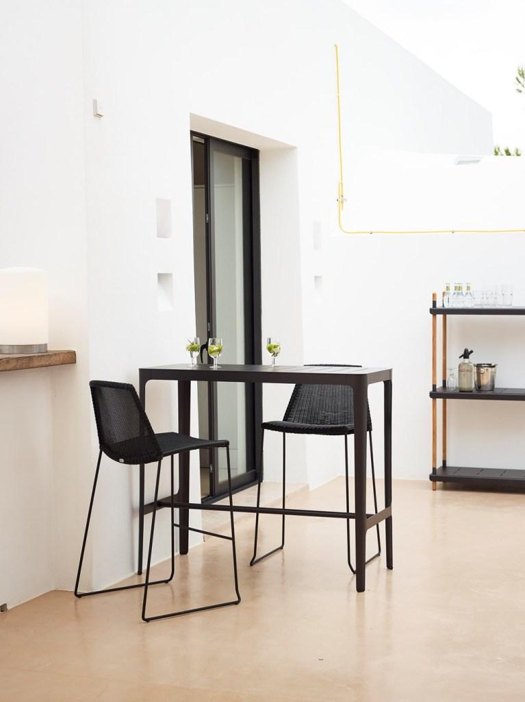 Dwa krzesła barowe z siedziskiem i oparciem ręcznie wyplatanym z włókna Cane-line Weave przy wysokim stole.