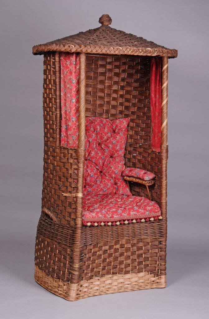 Fotel ogrodowy tzw. buda, kształt walca ze stożkowym zadaszeniem, czerwone poduszki ze wzorem w gałązki drobnych kwiatów.