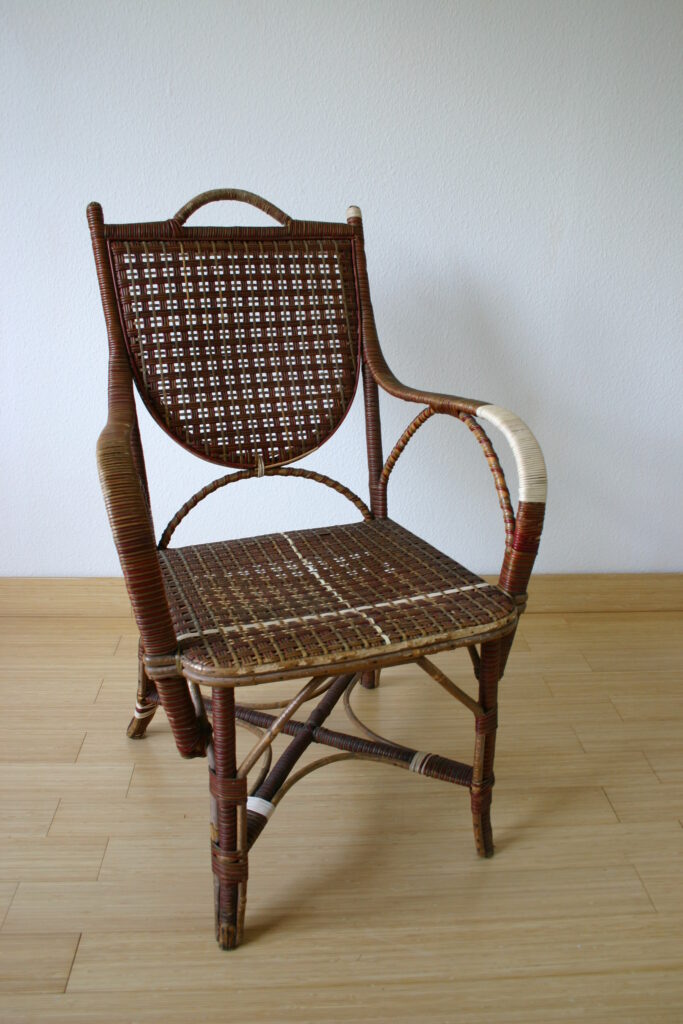 Fotel rattanowy wypleciony z kolorowych witek rattanowych - czerwone, brązowe i beżowe. Fotel na czterech nogach a podłokietnikami. Oparcie z misterną plecionką.