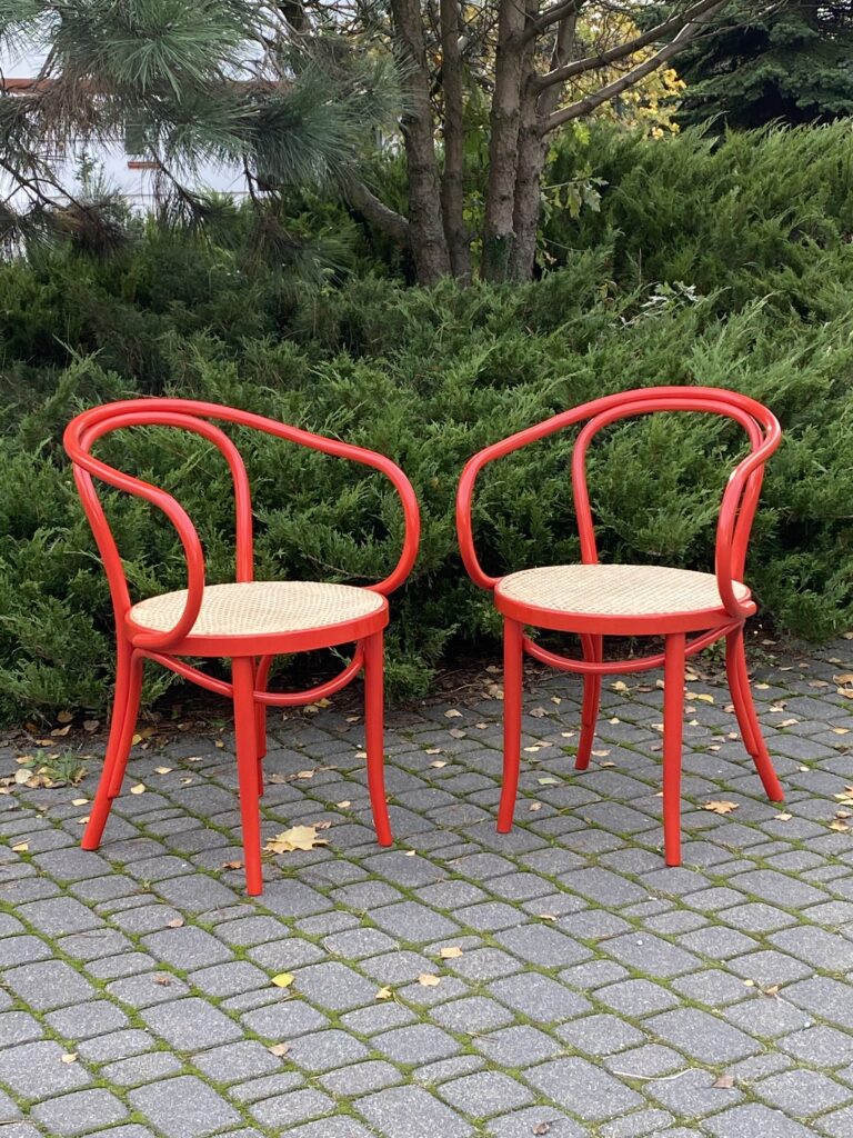 Widok na dwa krzesła gięte z plecionką rattanową, ramy krzeseł czerwone, jasna plecionka rattanowa