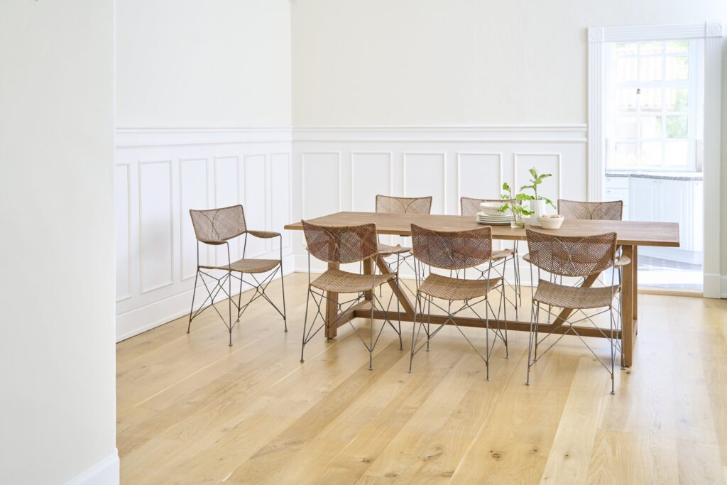 Krzesła RAP projekt Yuzura Yamakawa stoją przy drewnianym, prostokątnym stole. Siedem krzeseł z rattanu i metalowych konstrukcji tworzących ramę. Podłoga drewniana, ściany białe.