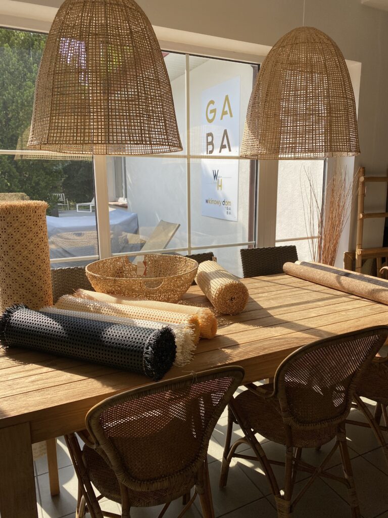 Zdjęcie z GABA 2 widok na fragment showroomu, stół tekowy, nad którym wiszą dwie duże lampy rattanowa, na stole leżą plecionki rattanowe w rolkach