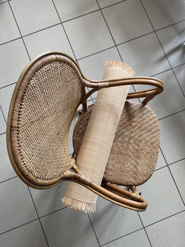 widok z góry na krzesło rattanowe, na którym leży rolka plecionki rattanowej, kolory beżowe, podłoga szara