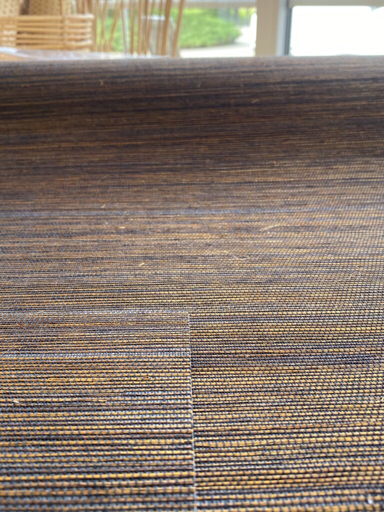 Zbliżenie na rozłożoną rolkę tapety z sizalu, tapeta mieni się różnymi kolorami ze złotymi refleksami