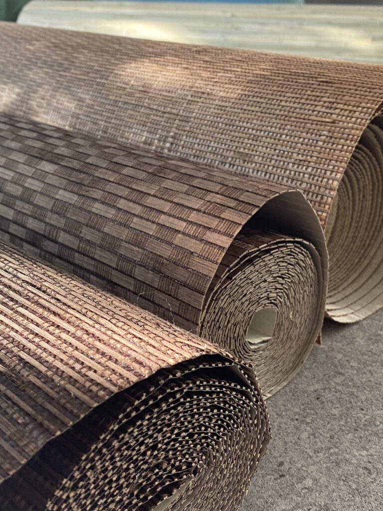 Trzy rolki tapet z bambusa w kolorze brązowym, leżą na drewnianym stole.