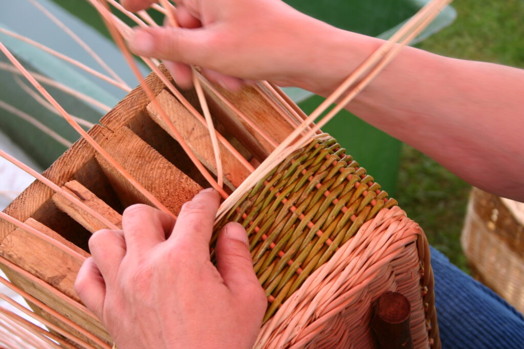 zbliżenie na ręce plecionkarza wyplatającego koszyk z wikliny, wyplatanie na drewnianej formie
