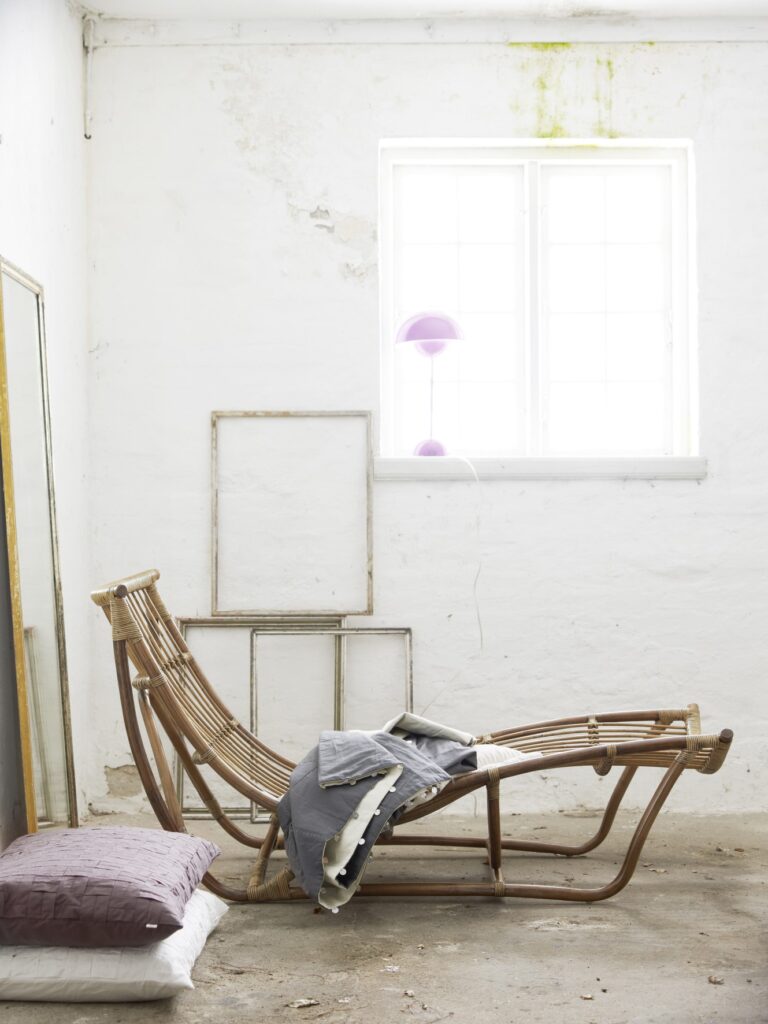 Leżanka rattanowa w kolorze naturalnym stoi w rustykalnym pomieszczeniu