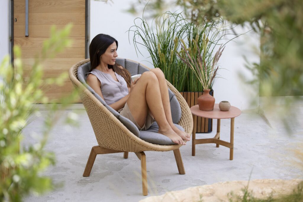 wygodny fotel outdoor, siedzi na nin młoda kobieta z podkurczonymi nogami