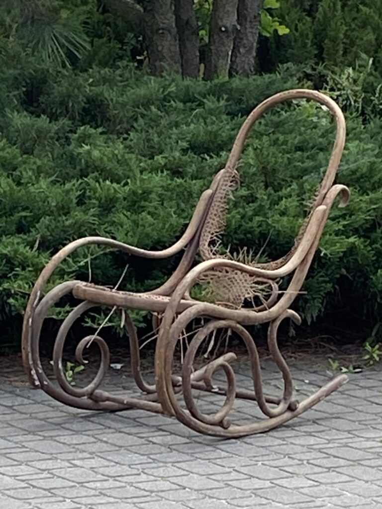 Na tle zielonych krzewów uszkodzony , stary fotel bujany.