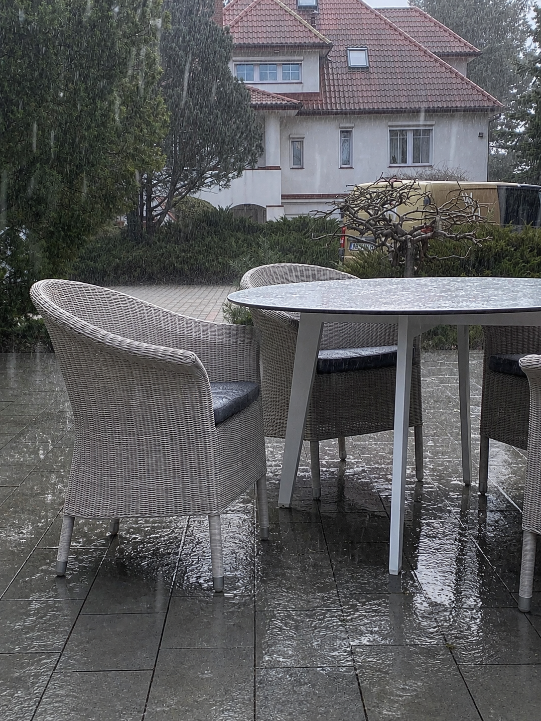 Meble z plecionki odpornej na wodę stoją na tarasie w czasie ulewy