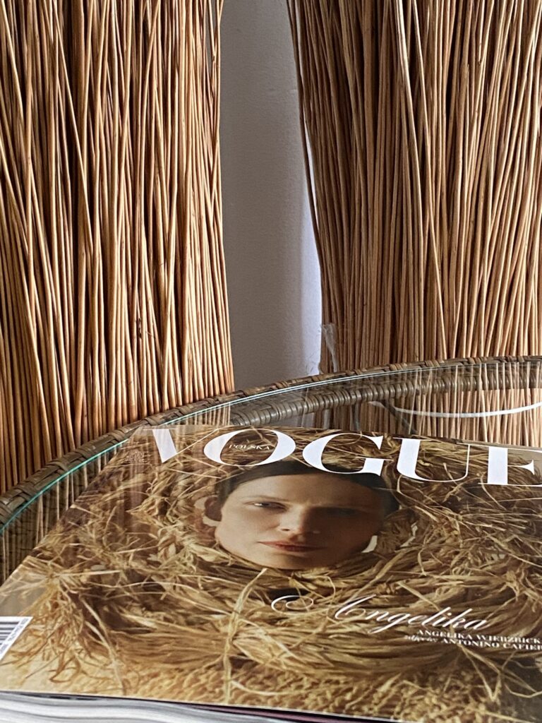 Miesięcznik Vogue leży na szklanym blacie stołu z wyplatanym rantem w tle wiązki wikliny