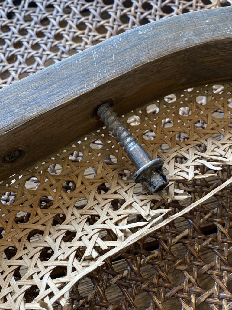 Uszkodzone siedzisko z plecionki rattanowej i śruba montażowa