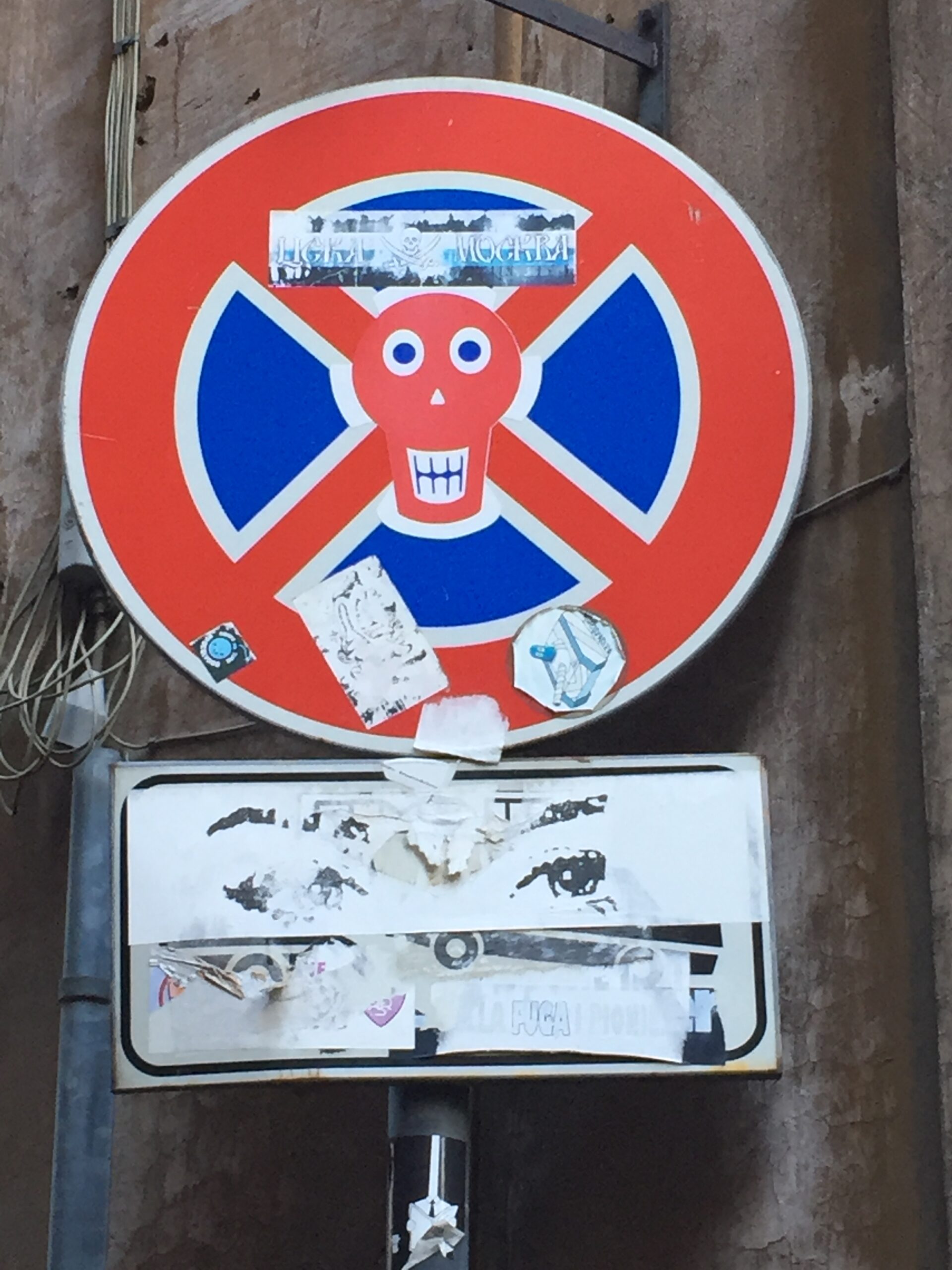 Znak drogowy w Rzymie pokryty naklejkami i śladami plakatów, ukazujący warstwowość miejskiej przestrzeni i kulturę uliczną.