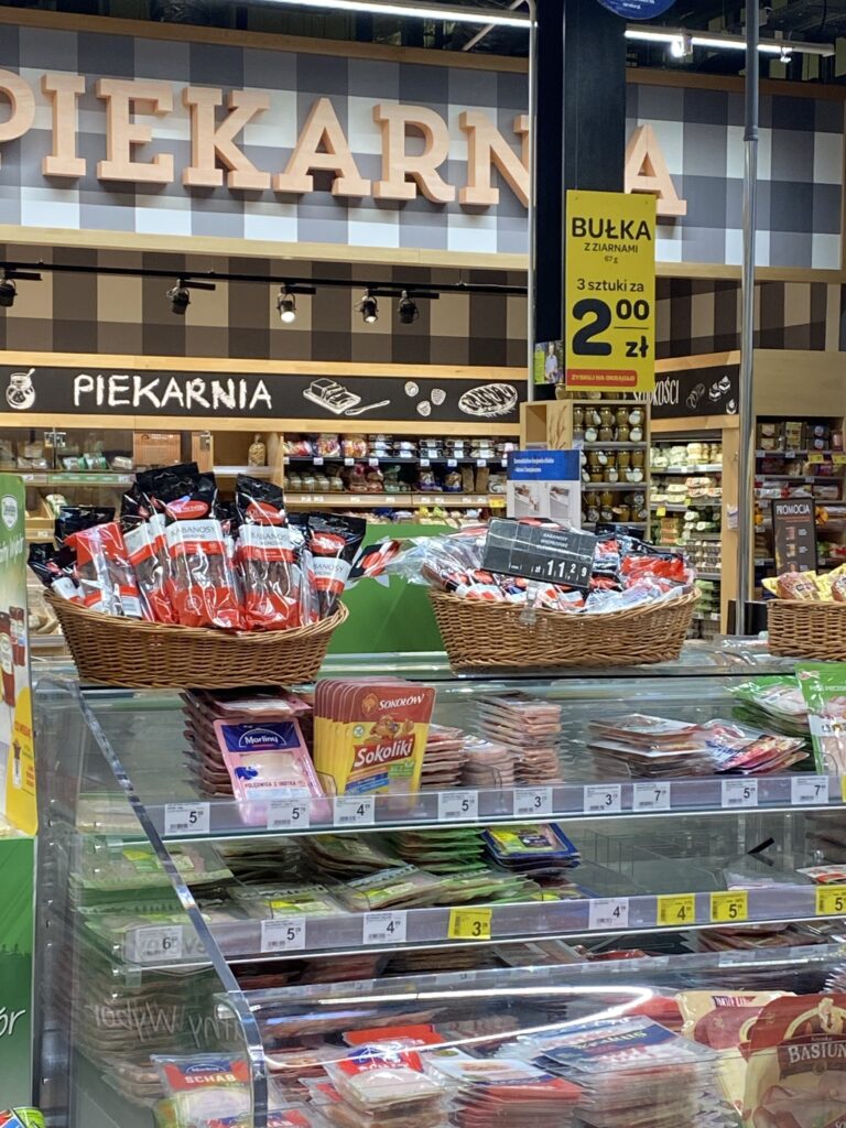 Płytkie wiklinowe kosze ekspozycyjne z produktami ustawione na ladzie chłodniczej w sklepie spożywczym jako element visual merchandisingu.
