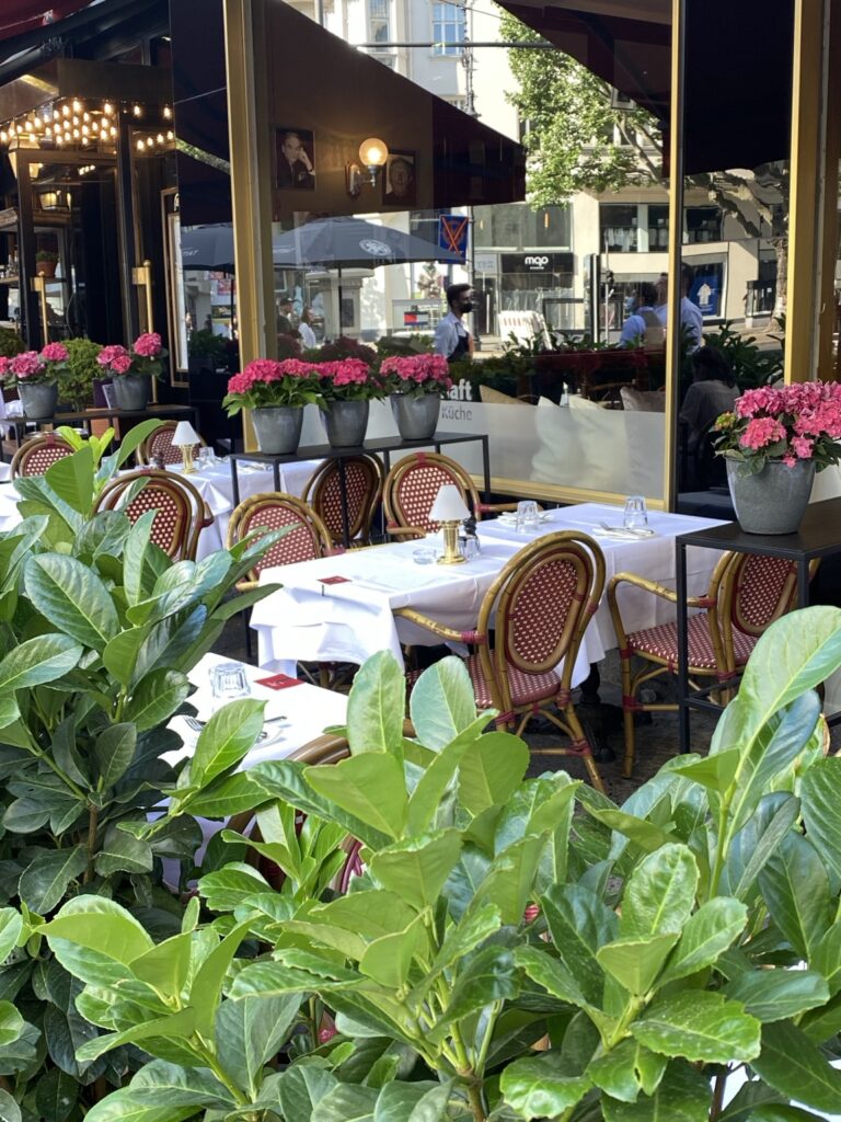 Ogródek restauracyjny z klasycznymi krzesłami w stylu paryskich kawiarni, białymi obrusami i hortensjami tworzącymi przyjazną przestrzeń miejską.